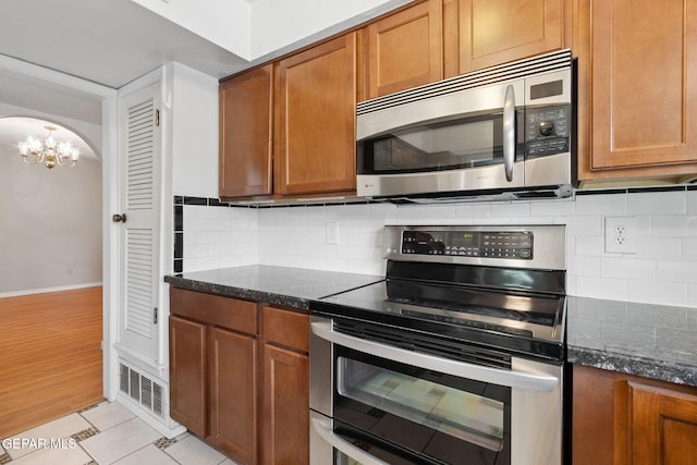 5536 Fernwood Cir, El Paso, TX 79932 - kitchen with stainless steel appliances, a chandelier, brown cabinetry, and dark stone countertops