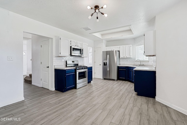 11948 Crown Oaks Ct, El Paso, TX 79936 - kitchen with appliances with stainless steel finishes, blue cabinets, a raised ceiling, light wood-style flooring, and tasteful backsplash