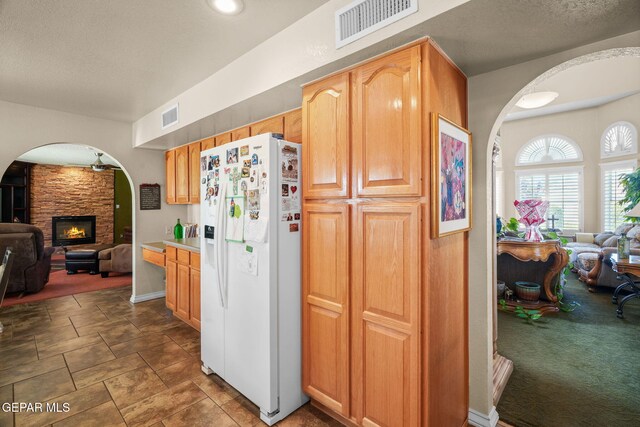 18986 Armington Dr, Horizon City, TX 79928 - kitchen with white fridge with ice dispenser, arched walkways, open floor plan, a stone fireplace, and stone finish flooring