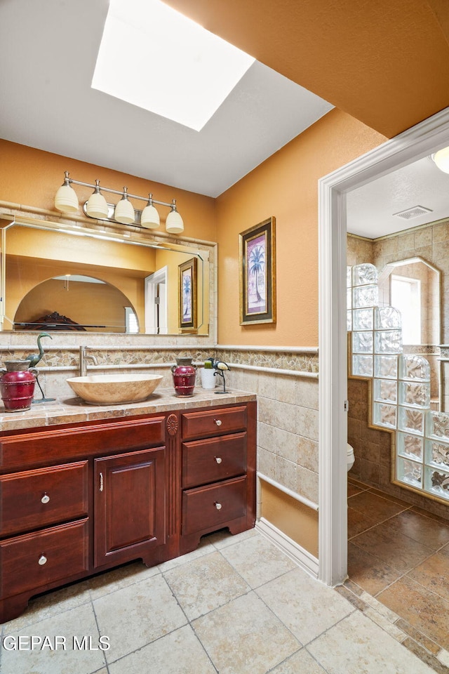 18986 Armington Dr, Horizon City, TX 79928 - bathroom with tile walls, a skylight, vanity, a wainscoted wall, and tile patterned flooring