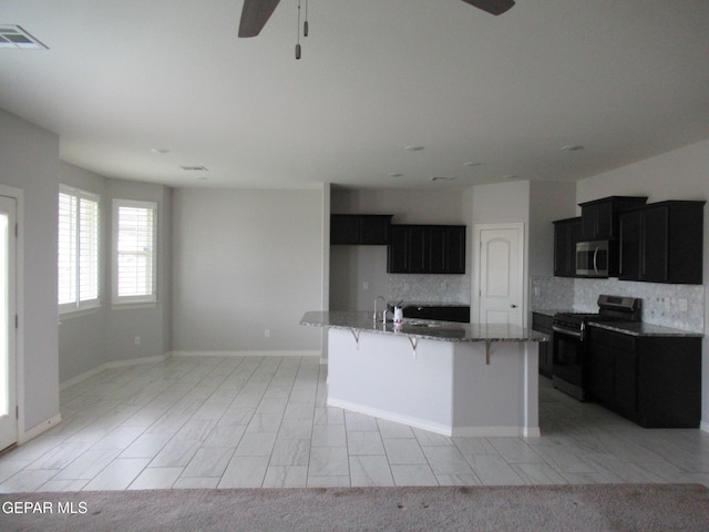 2813 Mike Price Dr, El Paso, TX 79938 - kitchen featuring stainless steel microwave, range with gas cooktop, ceiling fan, dark cabinetry, and tasteful backsplash