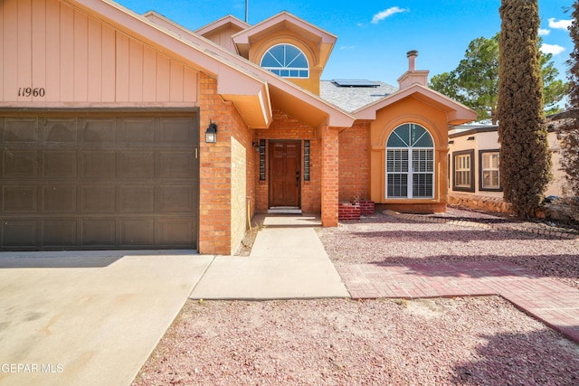 11960 Francis Scobee Dr, El Paso, TX 79936 - view of front facade with brick siding, concrete driveway, solar panels, an attached garage, and a chimney