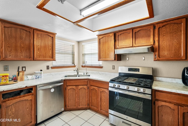 11960 Francis Scobee Dr, El Paso, TX 79936 - kitchen with stainless steel appliances, under cabinet range hood, light countertops, brown cabinets, and light tile patterned floors