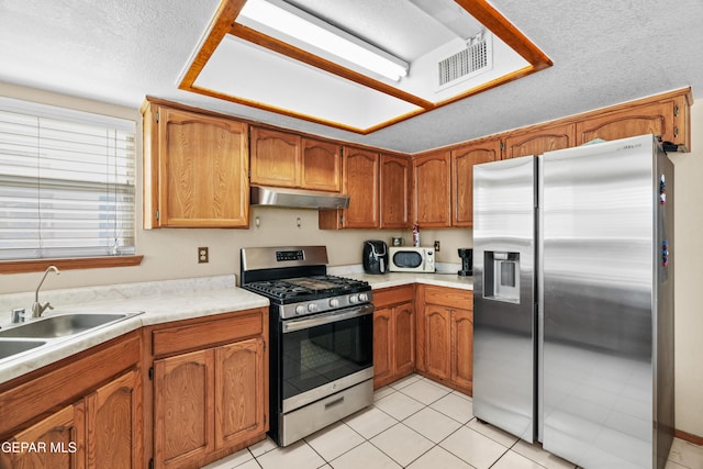 11960 Francis Scobee Dr, El Paso, TX 79936 - kitchen with appliances with stainless steel finishes, under cabinet range hood, brown cabinets, light countertops, and light tile patterned flooring