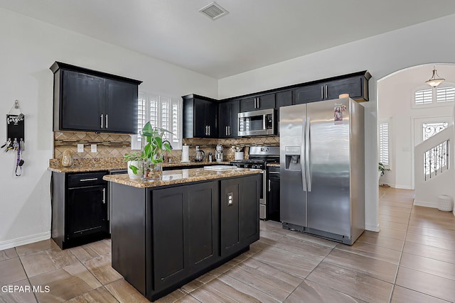 3143 Red Maple, El Paso, TX 79938 - kitchen with appliances with stainless steel finishes, tasteful backsplash, light stone counters, dark cabinets, and a kitchen island
