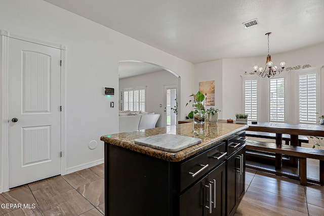 3143 Red Maple, El Paso, TX 79938 - kitchen featuring arched walkways, decorative light fixtures, dark cabinetry, a center island, and stone counters