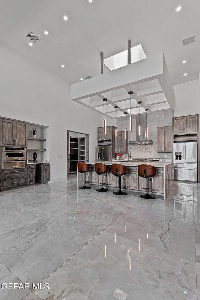 6325 Camino Pinon, El Paso, TX 79932 - kitchen featuring wall chimney exhaust hood, stainless steel appliances, a breakfast bar area, light countertops, and light marble finish floors