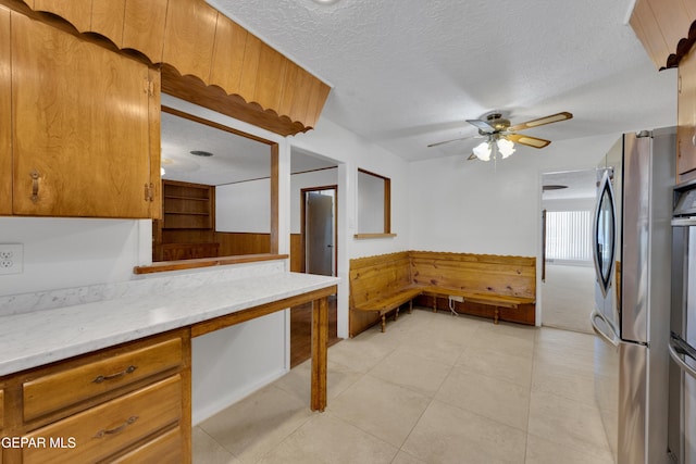 3313 Dublin Rd, El Paso, TX 79925 - kitchen featuring a wainscoted wall, a textured ceiling, ceiling fan, freestanding refrigerator, and wood walls
