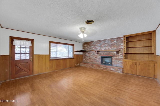 3313 Dublin Rd, El Paso, TX 79925 - unfurnished living room featuring wood finished floors, ceiling fan, a wainscoted wall, a textured ceiling, and a brick fireplace