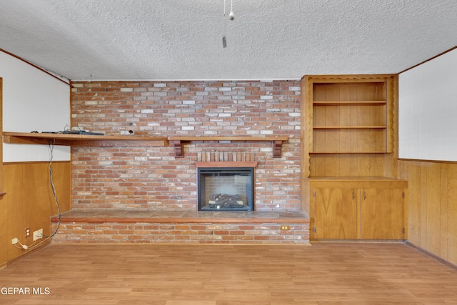 3313 Dublin Rd, El Paso, TX 79925 - unfurnished living room featuring a textured ceiling, wood finished floors, wood walls, built in features, and a brick fireplace