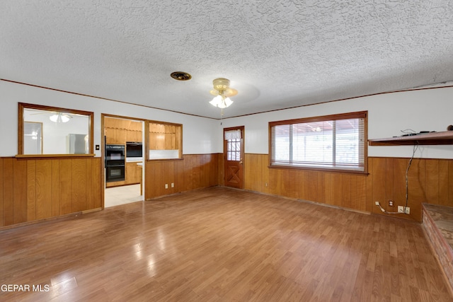 3313 Dublin Rd, El Paso, TX 79925 - unfurnished living room with a wainscoted wall, ceiling fan, light wood finished floors, wooden walls, and a textured ceiling