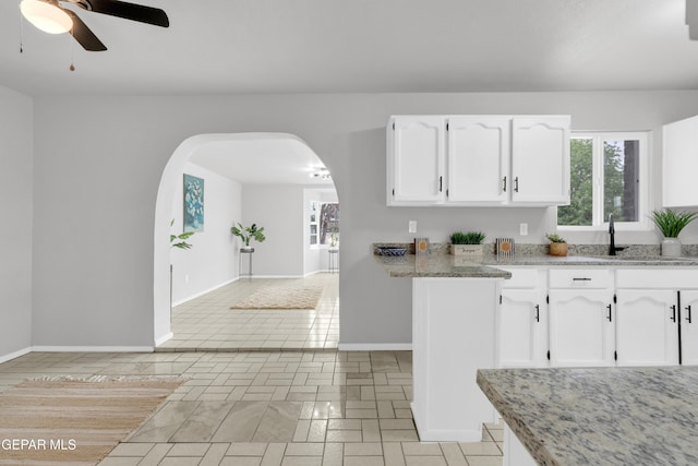 8936 Mount Rushmore Ln, El Paso, TX 79904 - kitchen with white cabinetry, arched walkways, ceiling fan, and light stone counters