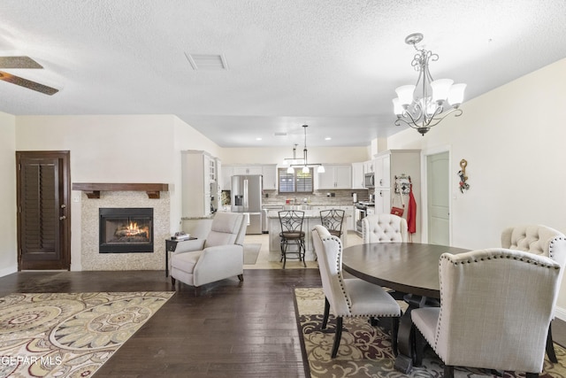 658 Sara Lynn Ct, El Paso, TX 79932 - dining room with dark wood-type flooring, a chandelier, a warm lit fireplace, a textured ceiling, and ceiling fan