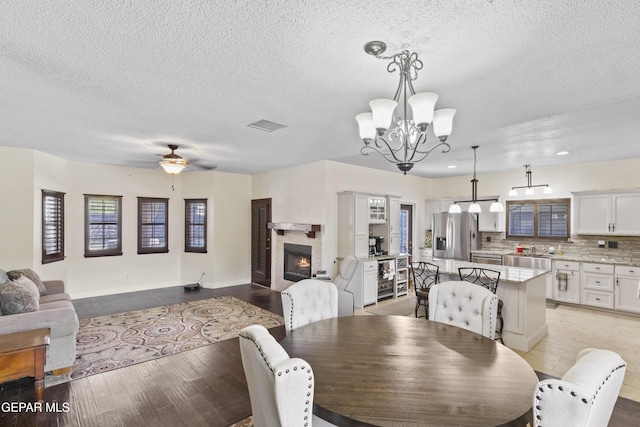 658 Sara Lynn Ct, El Paso, TX 79932 - dining room with a textured ceiling, a chandelier, a warm lit fireplace, ceiling fan, and light wood-style floors