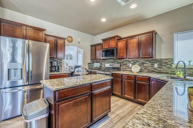 12616 Blazing Star Dr, El Paso, TX 79928 - kitchen with stainless steel appliances, arched walkways, light stone counters, a center island, and tasteful backsplash
