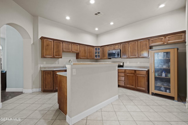 13788 Paseo Verde Dr, El Paso, TX 79928 - kitchen with stainless steel microwave, light tile patterned flooring, arched walkways, glass insert cabinets, and light countertops