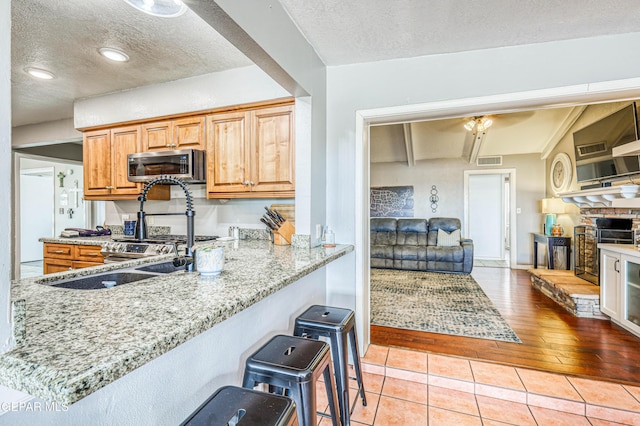 10705 Vista Alegre Dr, El Paso, TX 79935 - kitchen with stainless steel microwave, a textured ceiling, light stone counters, light tile patterned floors, and brown cabinetry