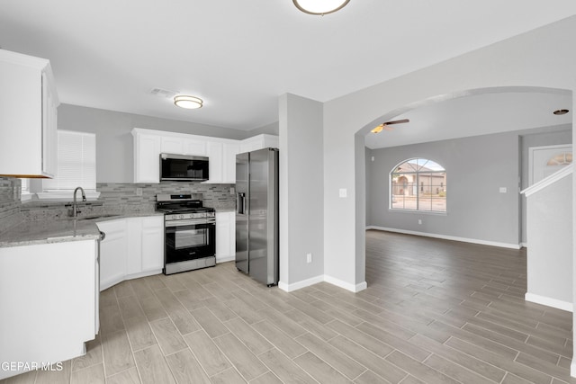 6913 Jericho Tree Dr, El Paso, TX 79934 - kitchen with stainless steel appliances, tasteful backsplash, arched walkways, light stone counters, and open floor plan