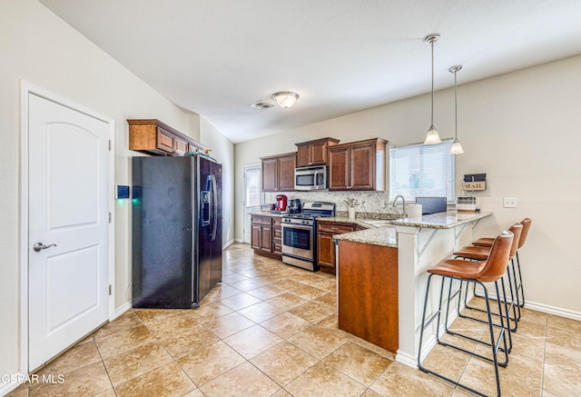 12257 Gaudi Way, El Paso, TX 79938 - kitchen with stainless steel appliances, a peninsula, a breakfast bar area, light stone counters, and hanging light fixtures