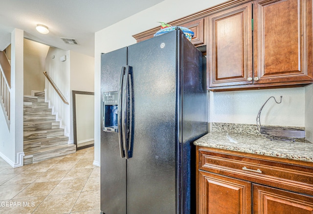 12257 Gaudi Way, El Paso, TX 79938 - kitchen with black fridge, light stone countertops, light tile patterned floors, and brown cabinets