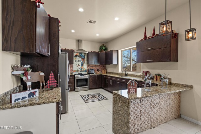 10728 Regina Dr, Socorro, TX 79927 - kitchen featuring appliances with stainless steel finishes, dark brown cabinets, wall chimney range hood, a peninsula, and light stone counters