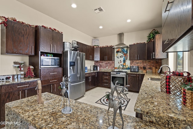 10728 Regina Dr, Socorro, TX 79927 - kitchen featuring stainless steel appliances, wall chimney exhaust hood, light stone countertops, tasteful backsplash, and dark brown cabinets