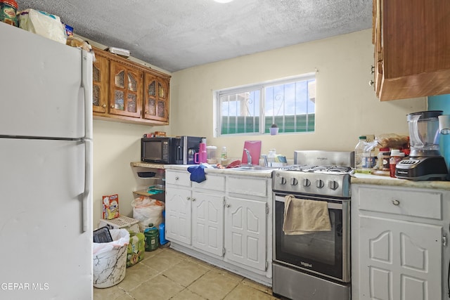 204 Ruth St, Anthony, NM 88021 - kitchen with freestanding refrigerator, stainless steel range with gas cooktop, light countertops, white cabinetry, and light tile patterned flooring