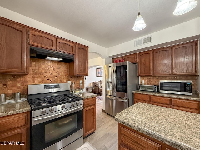 14177 Spanish Point Dr, El Paso, TX 79938 - kitchen with stainless steel appliances, under cabinet range hood, arched walkways, backsplash, and light wood-style flooring