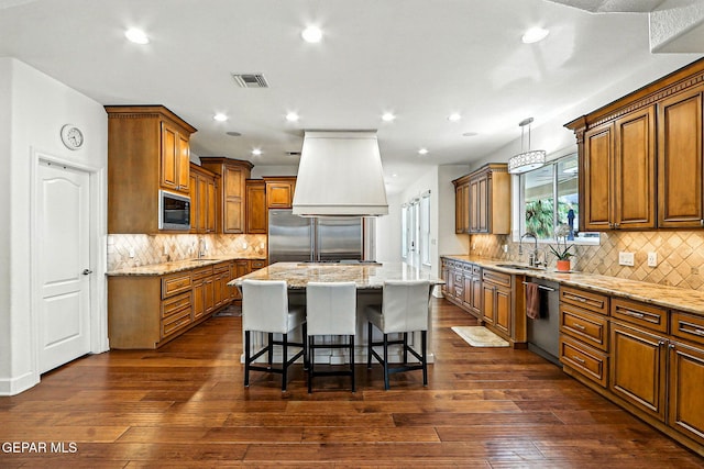 6528 Calle Placido Dr, El Paso, TX 79912 - kitchen with appliances with stainless steel finishes, a center island, brown cabinetry, premium range hood, and a kitchen breakfast bar