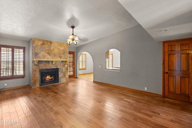 11852 Pete Rose Dr, El Paso, TX 79936 - unfurnished living room with a textured ceiling, plenty of natural light, a fireplace, wood finished floors, and arched walkways