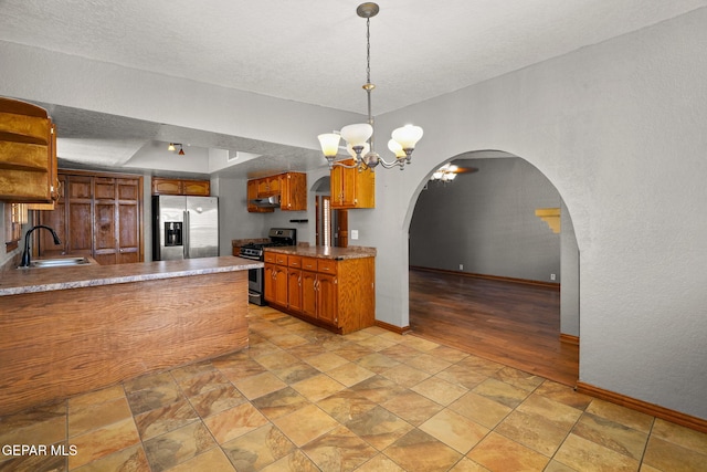 11852 Pete Rose Dr, El Paso, TX 79936 - kitchen with appliances with stainless steel finishes, arched walkways, brown cabinetry, a chandelier, and light stone finish flooring