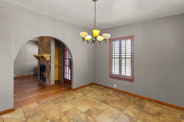 11852 Pete Rose Dr, El Paso, TX 79936 - empty room with a chandelier, a tile fireplace, a textured ceiling, arched walkways, and light stone finish floors