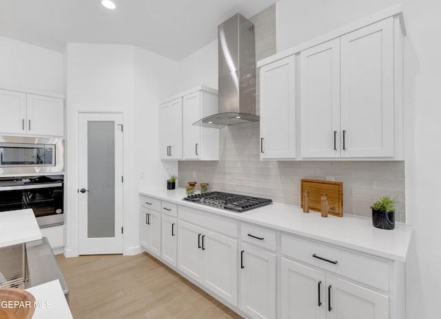141 Bonnie Trl, Sunland Park, NM 88063 - kitchen with wall chimney exhaust hood, appliances with stainless steel finishes, tasteful backsplash, white cabinets, and light wood-type flooring