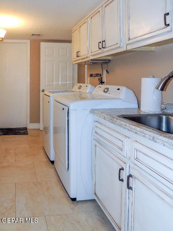 10945 Gary Player Dr, El Paso, TX 79935 - laundry area featuring washing machine and dryer, cabinet space, and light tile patterned flooring