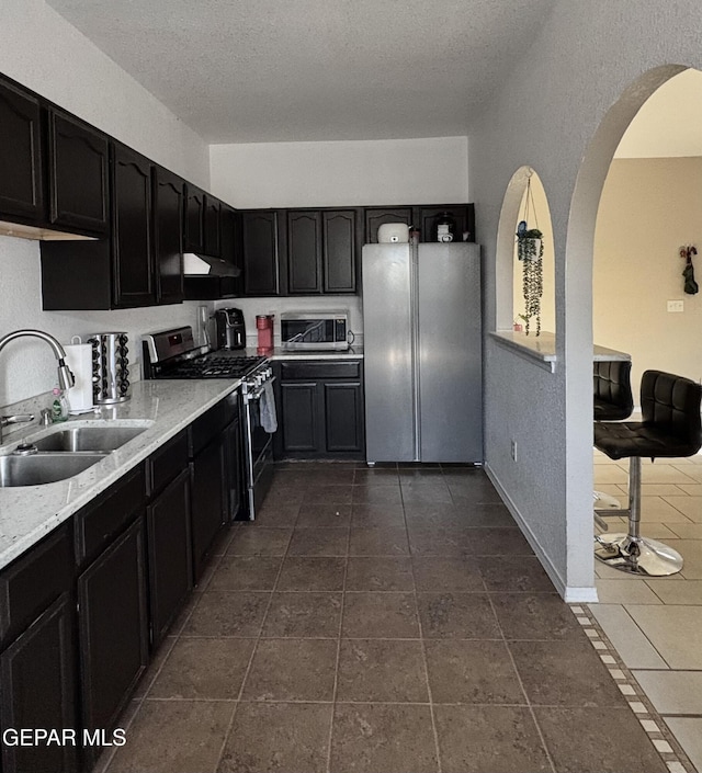 632 Manzanilla Pl, El Paso, TX 79928 - kitchen featuring appliances with stainless steel finishes, dark cabinets, a textured ceiling, under cabinet range hood, and arched walkways