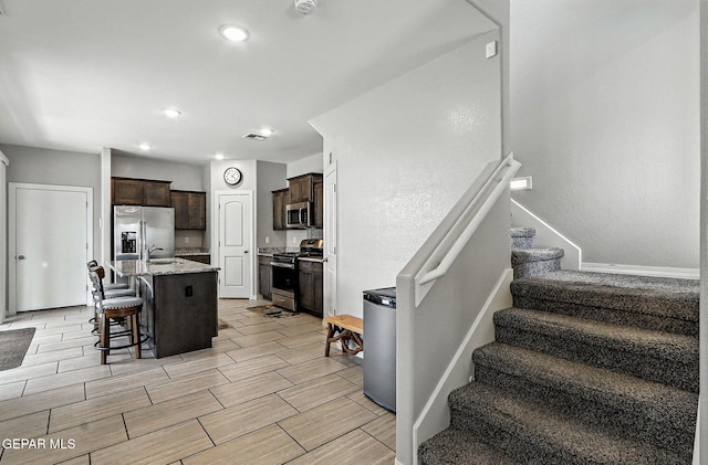 2116 Tim Foster St, El Paso, TX 79938 - kitchen with appliances with stainless steel finishes, dark brown cabinetry, a breakfast bar, light stone countertops, and wood finish floors