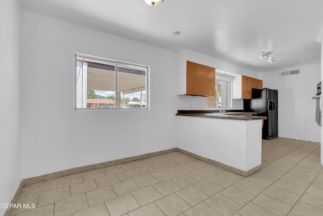 6033 Isabella Dr, El Paso, TX 79912 - kitchen with black fridge, dark countertops, a peninsula, stainless steel oven, and light tile patterned flooring
