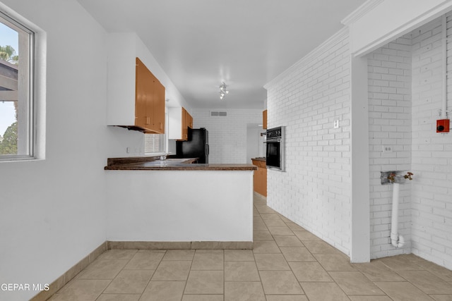 6033 Isabella Dr, El Paso, TX 79912 - kitchen with black appliances, healthy amount of natural light, dark countertops, brick wall, and a peninsula
