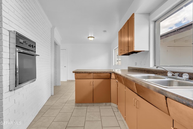 6033 Isabella Dr, El Paso, TX 79912 - kitchen featuring oven, brick wall, light tile patterned floors, and a peninsula
