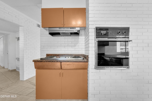 6033 Isabella Dr, El Paso, TX 79912 - kitchen with oven, stainless steel cooktop, light tile patterned flooring, under cabinet range hood, and dark countertops