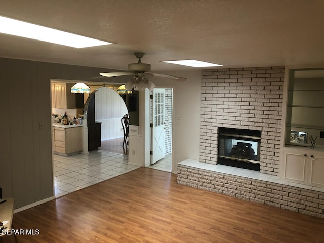 10309 Woodruff Ct, El Paso, TX 79925 - unfurnished living room featuring wood finished floors, ceiling fan, a brick fireplace, and a textured ceiling