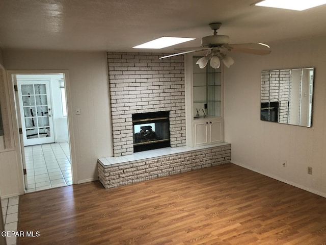 10309 Woodruff Ct, El Paso, TX 79925 - unfurnished living room with a brick fireplace, wood finished floors, ceiling fan, and a skylight