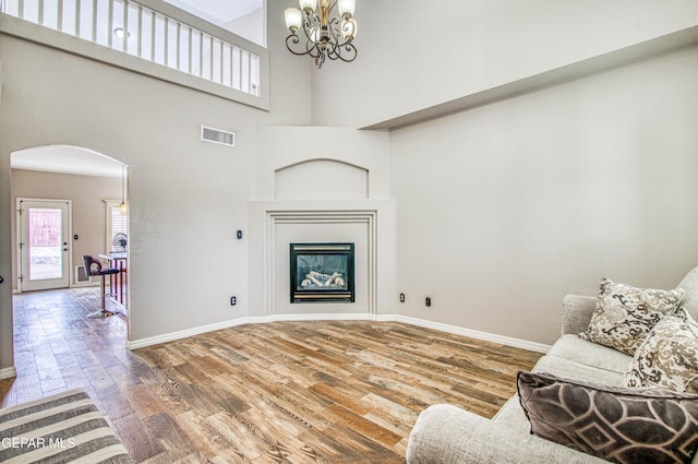 11813 Deer Grass Cir, El Paso, TX 79936 - living area with arched walkways, wood finished floors, a chandelier, a towering ceiling, and a glass covered fireplace
