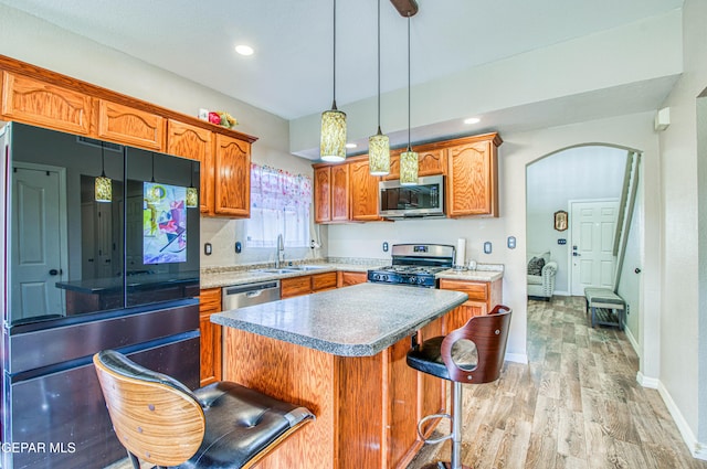 11813 Deer Grass Cir, El Paso, TX 79936 - kitchen featuring appliances with stainless steel finishes, arched walkways, light wood-style floors, brown cabinetry, and a kitchen breakfast bar
