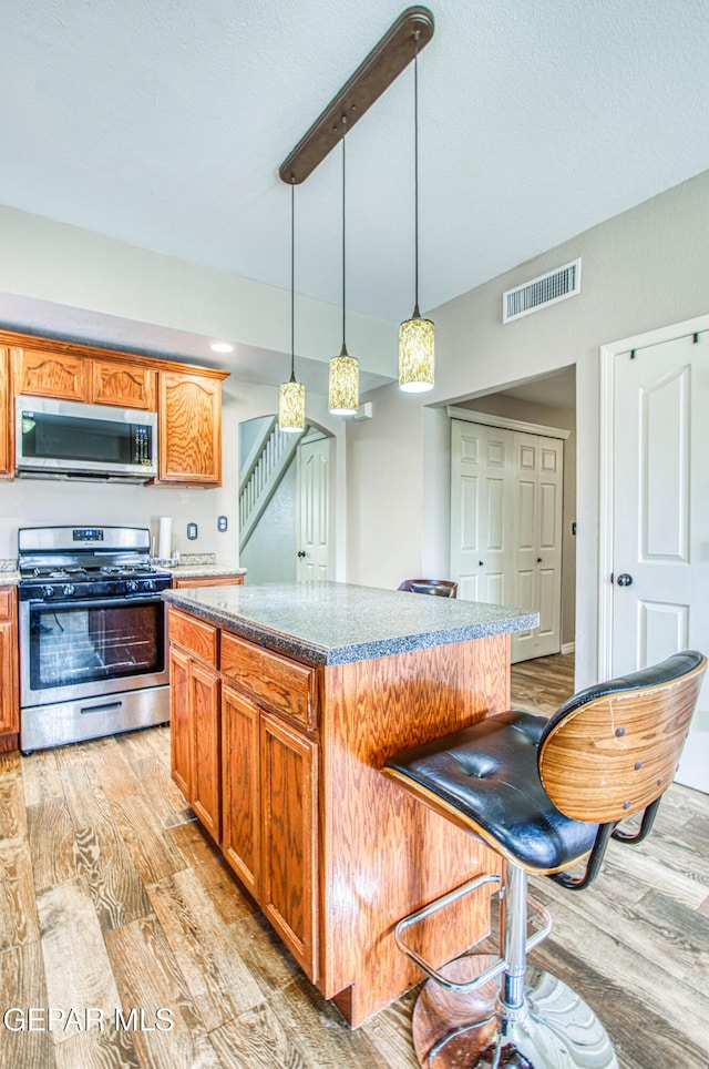 11813 Deer Grass Cir, El Paso, TX 79936 - kitchen with appliances with stainless steel finishes, light wood-style floors, a center island, and decorative light fixtures