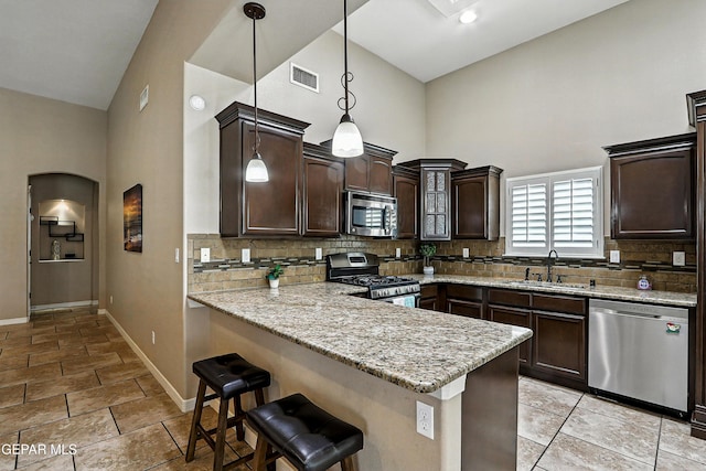 14552 Long Shadow Ave, El Paso, TX 79938 - kitchen with appliances with stainless steel finishes, a towering ceiling, a breakfast bar, dark brown cabinetry, and backsplash