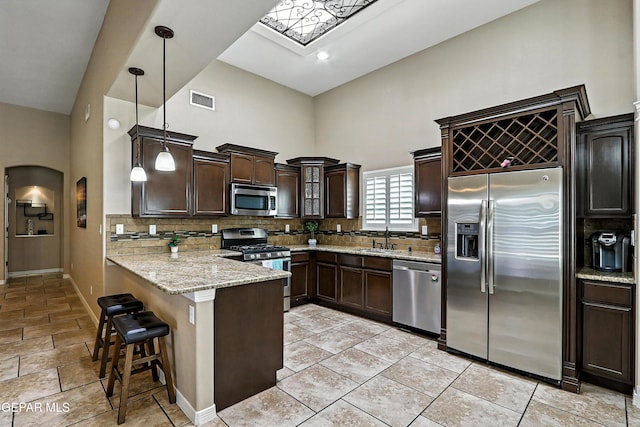 14552 Long Shadow Ave, El Paso, TX 79938 - kitchen with appliances with stainless steel finishes, a peninsula, dark brown cabinets, a high ceiling, and decorative backsplash