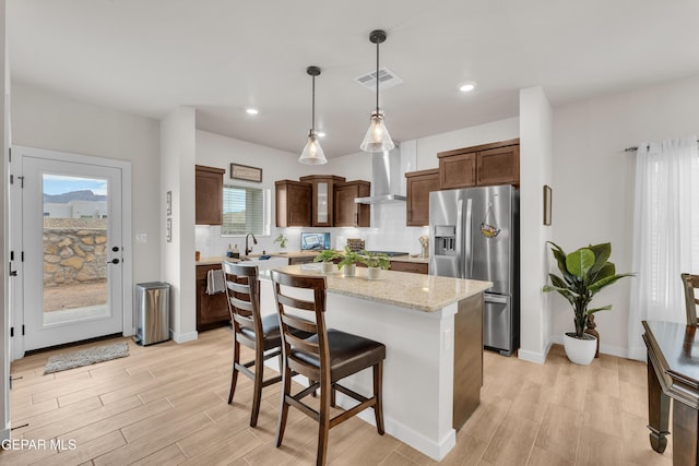 11157 Blazing Star Pl, El Paso, TX 79934 - kitchen with stainless steel appliances, wall chimney exhaust hood, a center island, decorative light fixtures, and light wood-style flooring