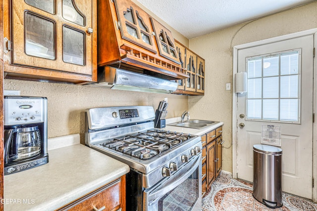11581 Valle Verde Rd, Socorro, TX 79927 - kitchen featuring stainless steel gas range, brown cabinets, light countertops, glass insert cabinets, and a textured ceiling