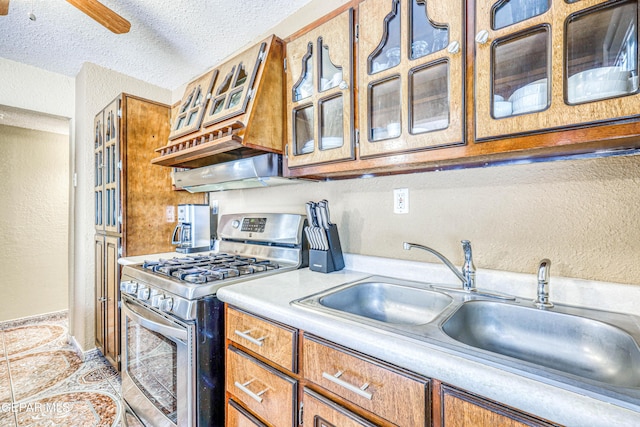 11581 Valle Verde Rd, Socorro, TX 79927 - kitchen featuring stainless steel gas range oven, light countertops, brown cabinets, a textured wall, and glass insert cabinets